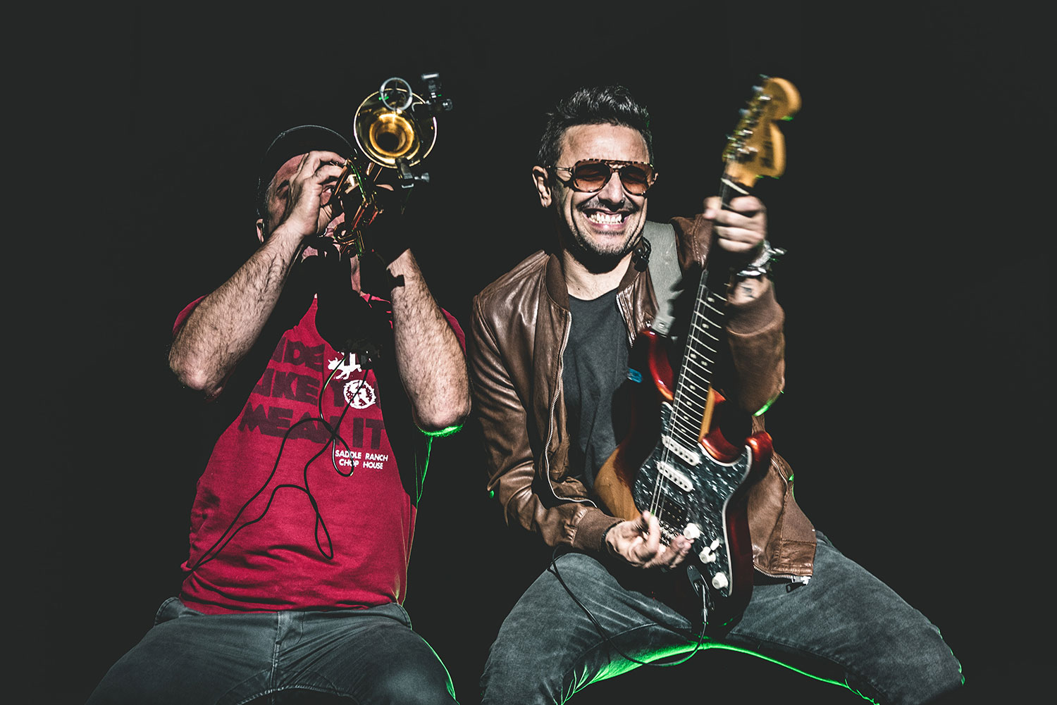 Integrantes de la banda No Te Va Gustar en una presentación en vivo. Uno toca la trompeta con energía, mientras el otro sonríe y toca una guitarra eléctrica, transmitiendo entusiasmo y pasión por la música.