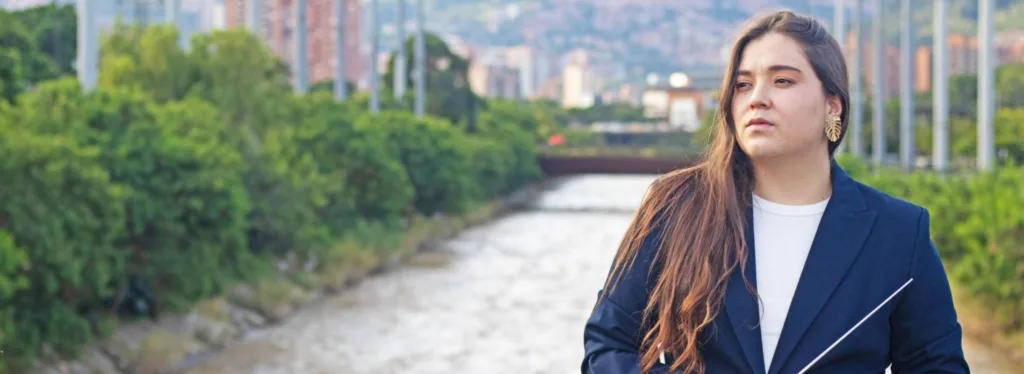 Ana María Patiño-Osorio, nueva directora titular de la Orquesta Filarmónica de Medellín, posando junto al río Medellín con batuta en mano.