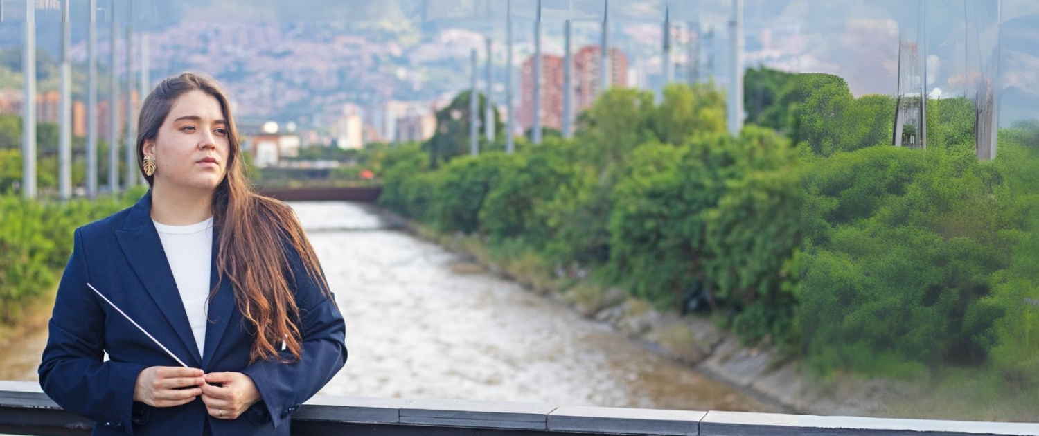 Ana María Patiño-Osorio, nueva directora titular de la Orquesta Filarmónica de Medellín, posando junto al río Medellín con batuta en mano.