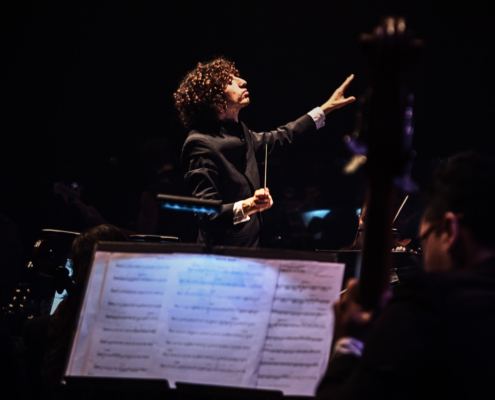 Director de orquesta guiando apasionadamente a músicos durante un concierto sinfónico en escenario oscuro.