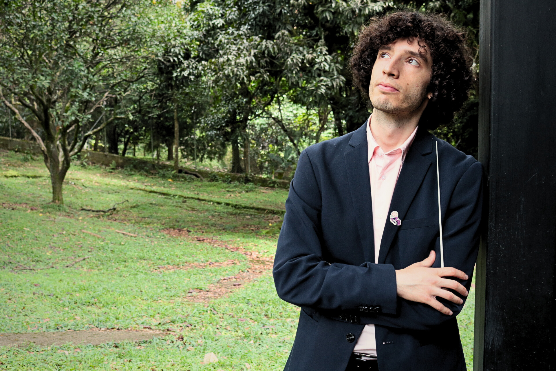 Tami Daniel Rueda-Blanco, director asociado de la Filarmónica de Medellín, posa pensativo al aire libre con batuta en mano