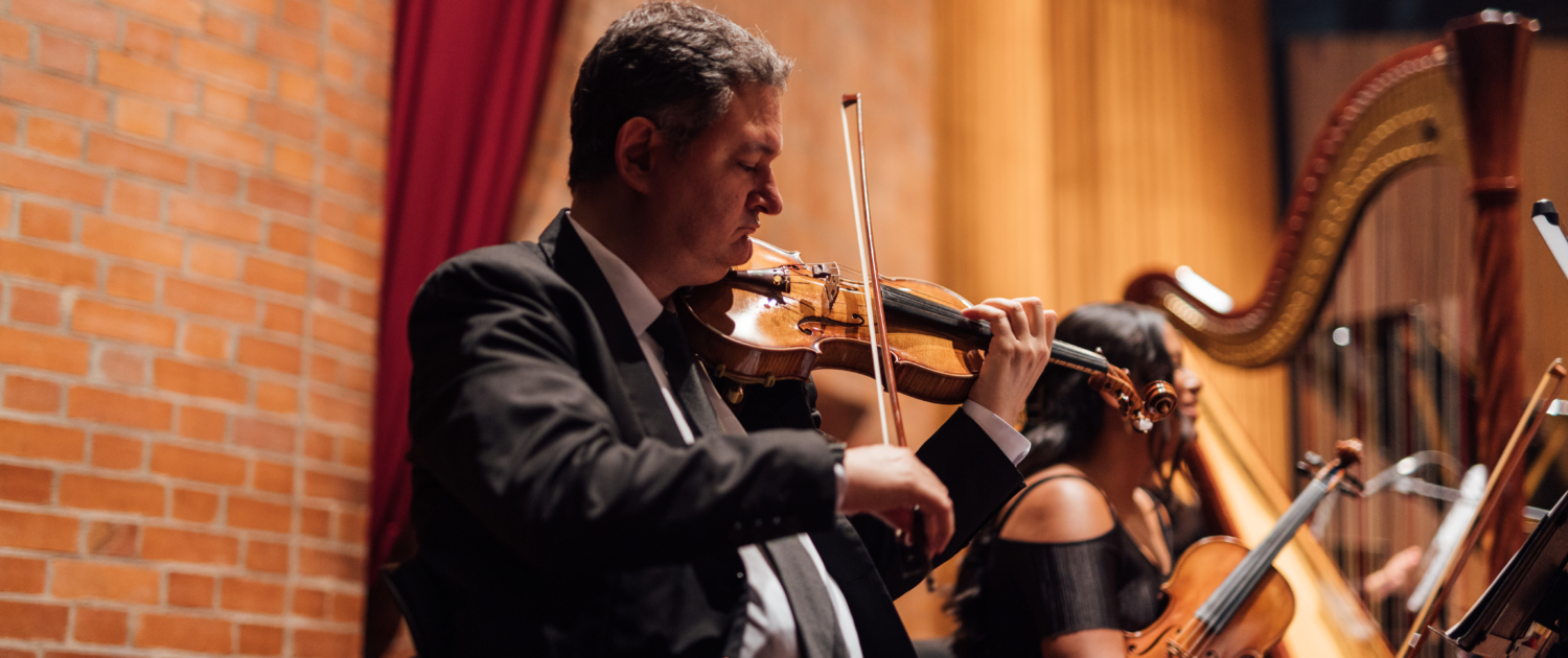 Violinista en traje formal interpretando música en una orquesta sinfónica junto a otros músicos