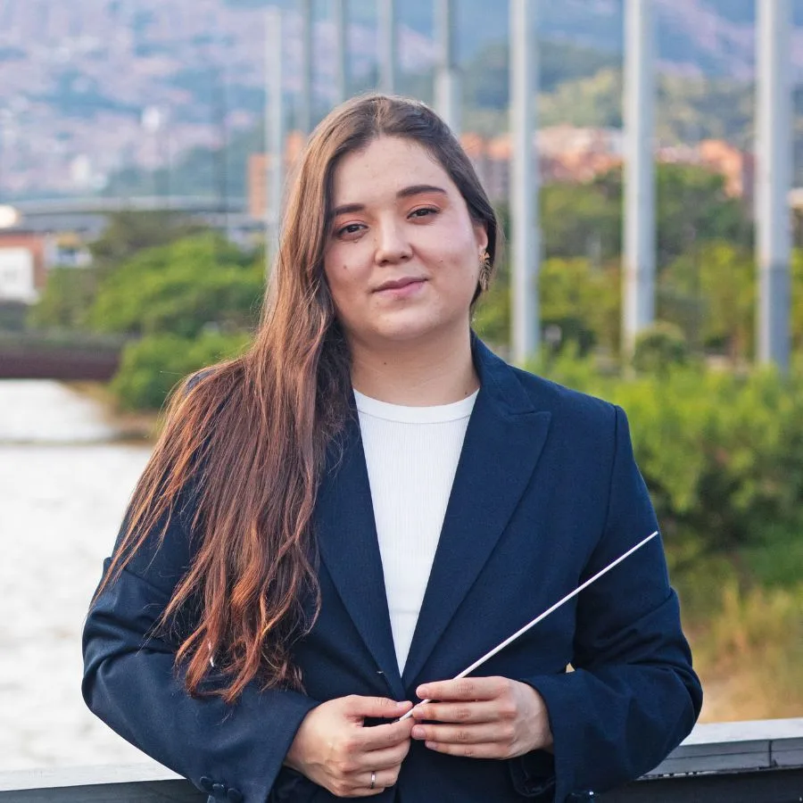 Ana María Patiño, directora titular de la Orquesta Filarmónica, al aire libre con fondo urbano y natural.