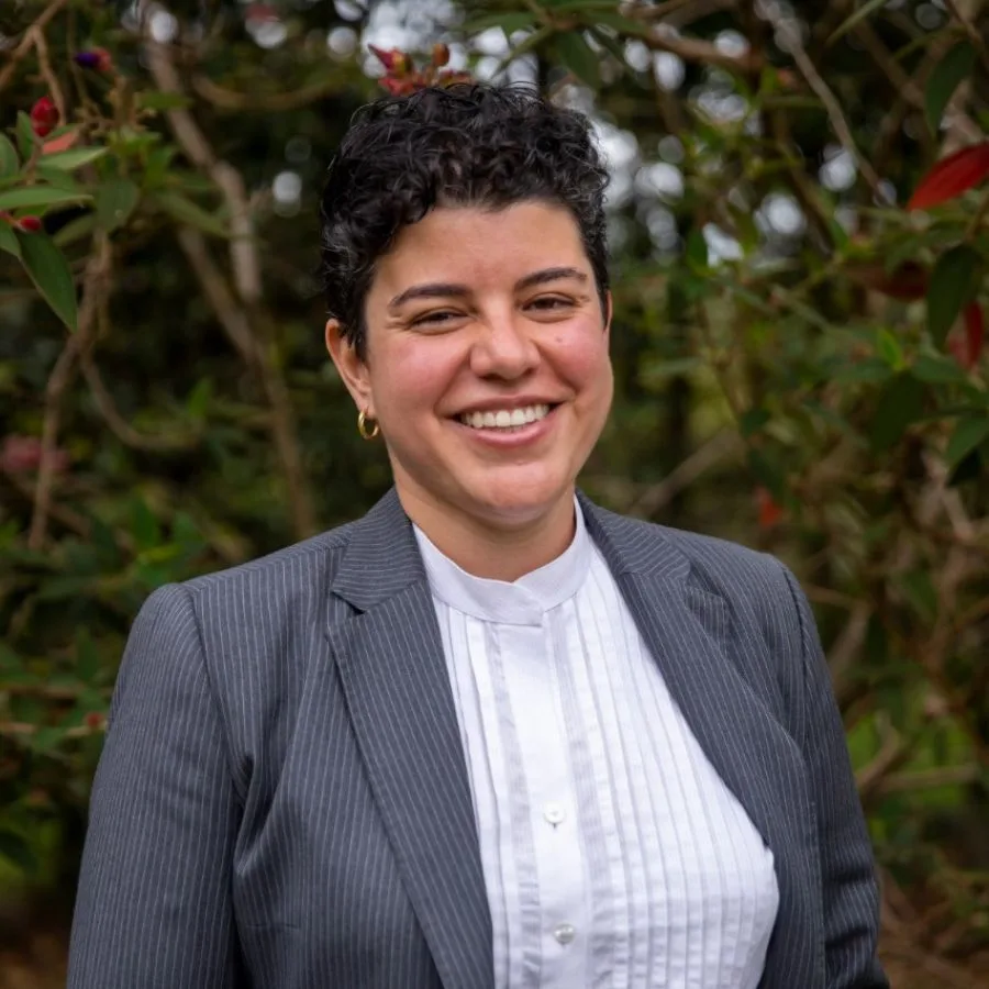 Catalina Prieto, directora ejecutiva de la orquesta filarmónica, sonriendo con traje formal frente a un fondo natural.