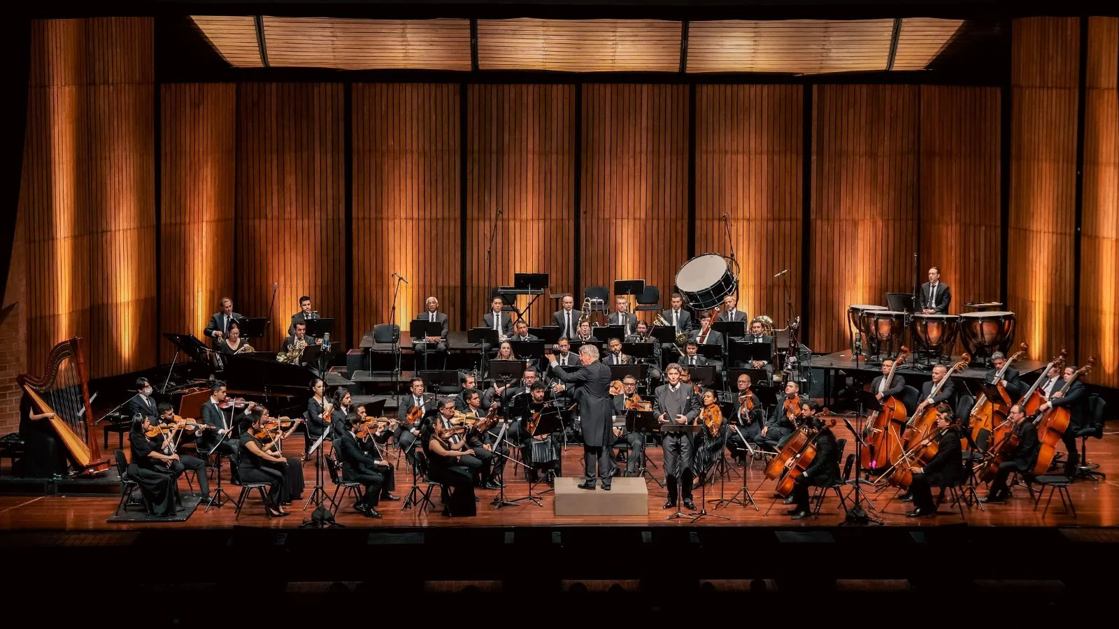 Orquesta Filarmónica de Medellín interpretando una obra sinfónica en un auditorio con iluminación cálida