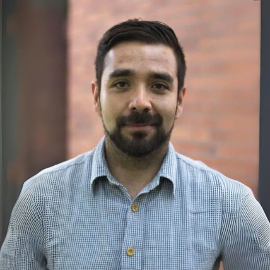 Felipe Vélez, responsable de gestión orquestal en la orquesta filarmónica, posando con camisa de cuadros frente a un fondo de ladrillo.