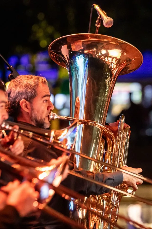 Músico de la Orquesta Filarmónica de Medellín tocando una tuba durante un concierto nocturno con iluminación cálida