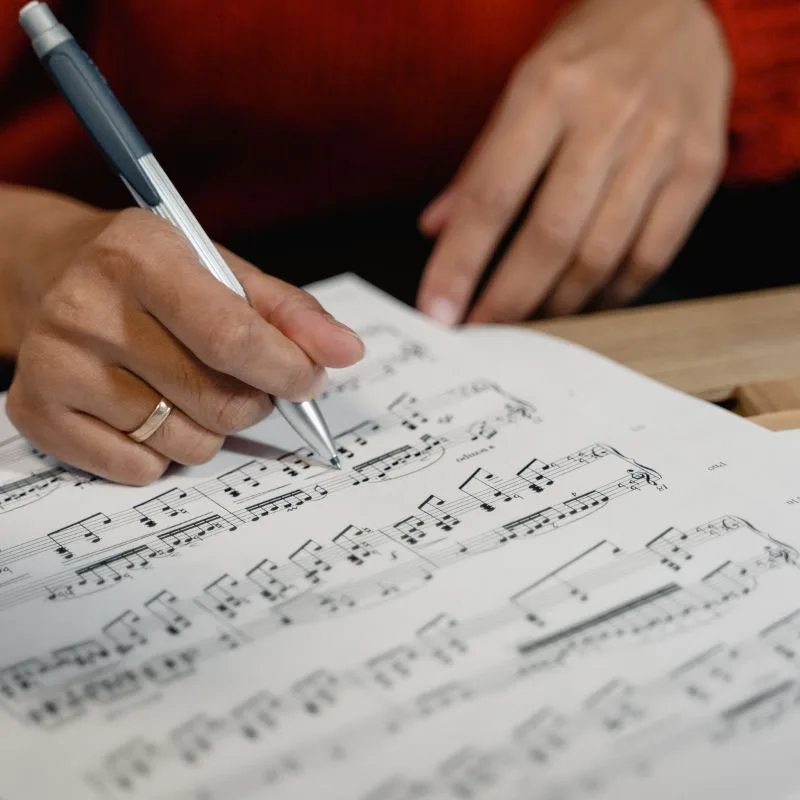 Manos de una persona haciendo anotaciones en una partitura musical con bolígrafo sobre una mesa