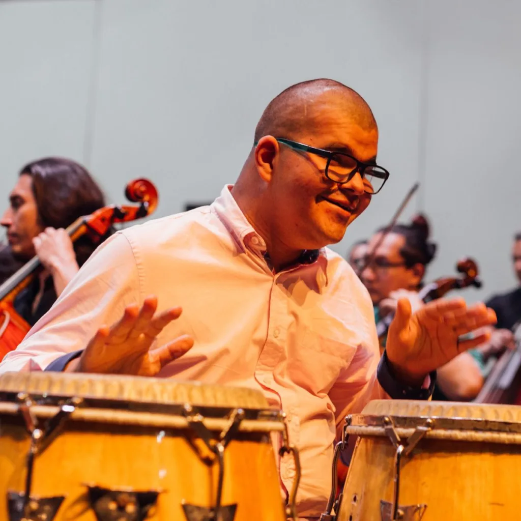 Hombre con discapacidad cognitiva toca congas durante presentación musical inclusiva junto a una orquesta.