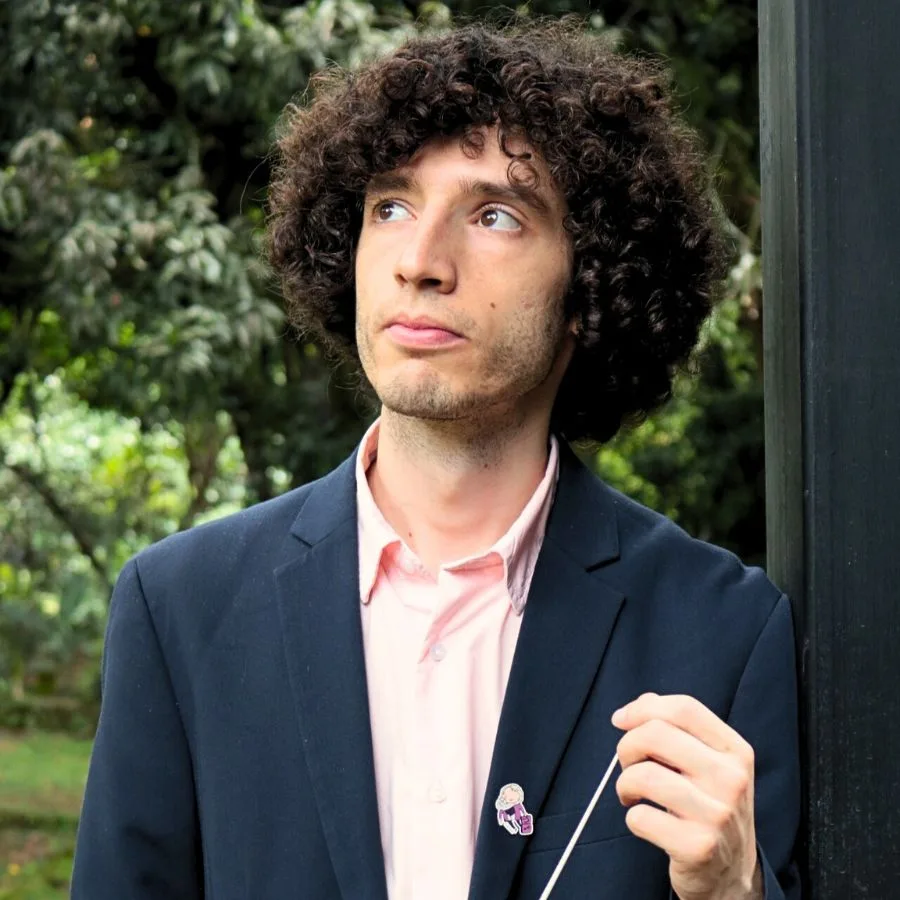 Tami Daniel Rueda, director asociado de orquesta, sosteniendo una batuta en un entorno natural.