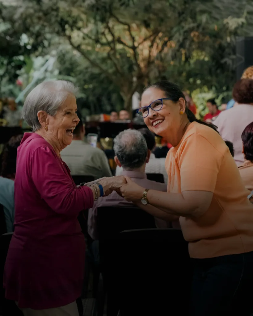 Dos mujeres sonríen y se toman de las manos durante un concierto al aire libre, como parte de la Retreta PoblemoS en el Parque de Orquídeas, La Presidenta.
