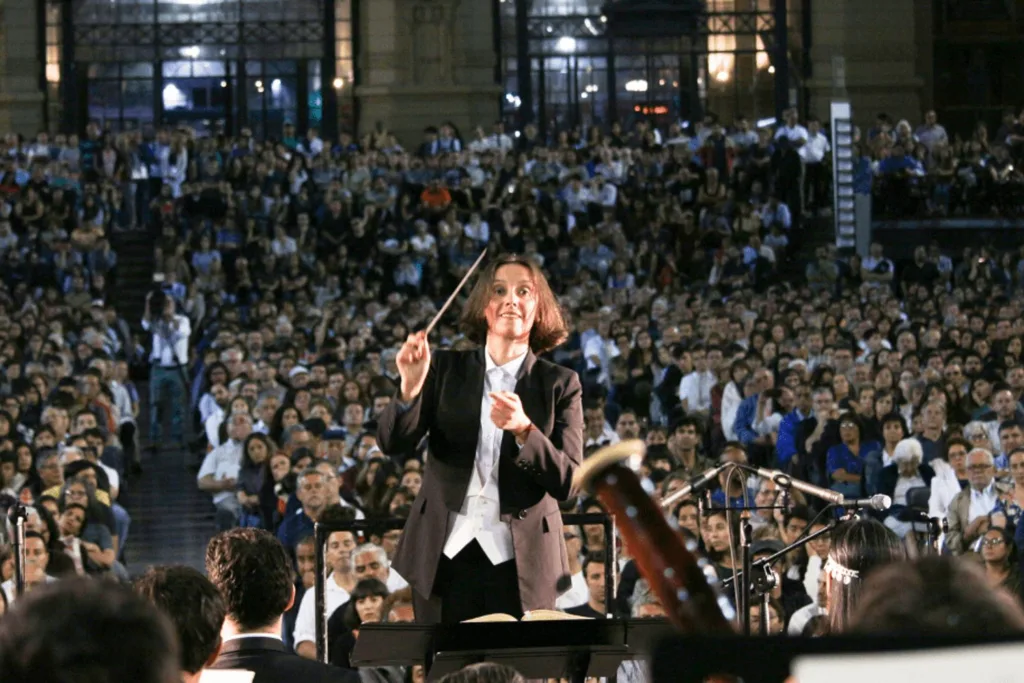 Alejandra Urrutia dirigiendo una orquesta frente a una multitud en un concierto al aire libre