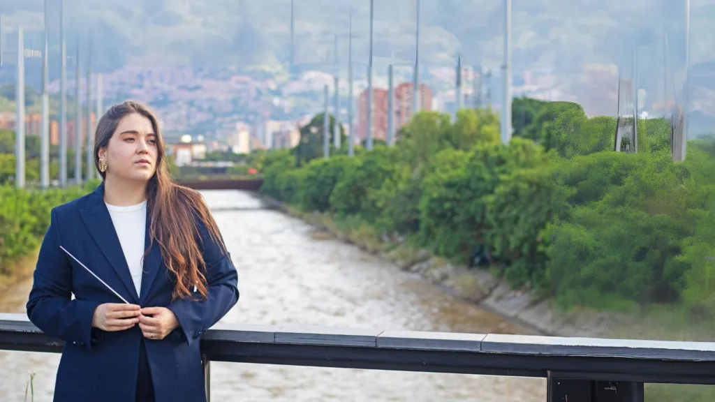 Ana María Patiño-Osorio, nueva directora titular de la Orquesta Filarmónica de Medellín, posando junto al río Medellín con batuta en mano.