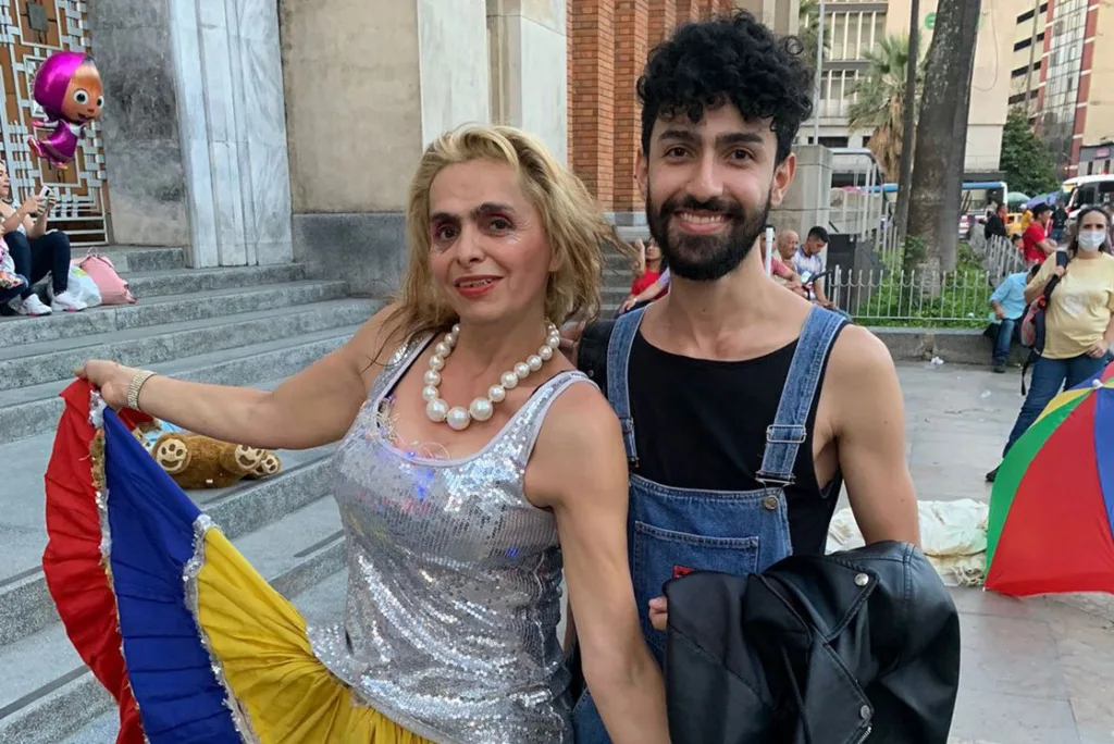 Camilo Martínez junto a una artista de teatro de calle con vestuario brillante y bandera de Colombia en espacio público del centro de Medellín.