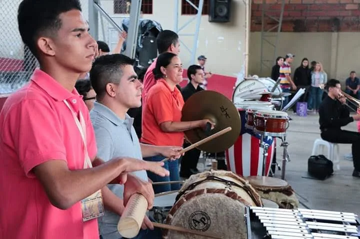 Grupo de percusionistas durante ensayo en Ciudad Bolívar; Jhon Freddy, con camisa gris, participa activamente tocando un instrumento tradicional.