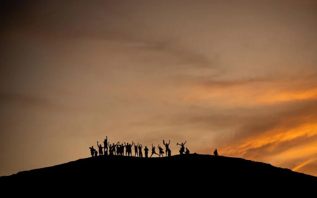 Grupo de personas celebrando sobre una colina en La Guajira, vistos en silueta contra un atardecer anaranjado y dorado, símbolo de comunidad, unión y esperanza.