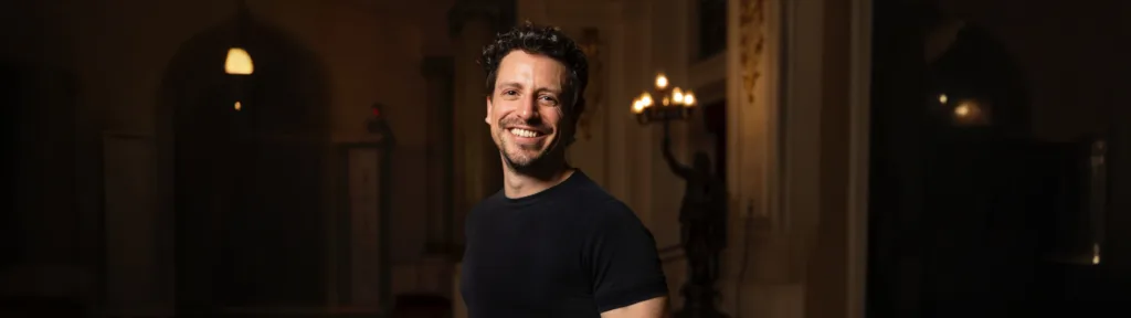 Paolo Bortolameolli sonriendo en un teatro iluminado, vestido con camiseta negra