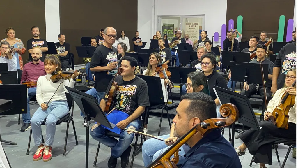 Personas de una empresa participan en un taller de liderazgo ofrecido por la Orquesta Filarmónica de Medellín, donde se integran a una experiencia musical guiada.