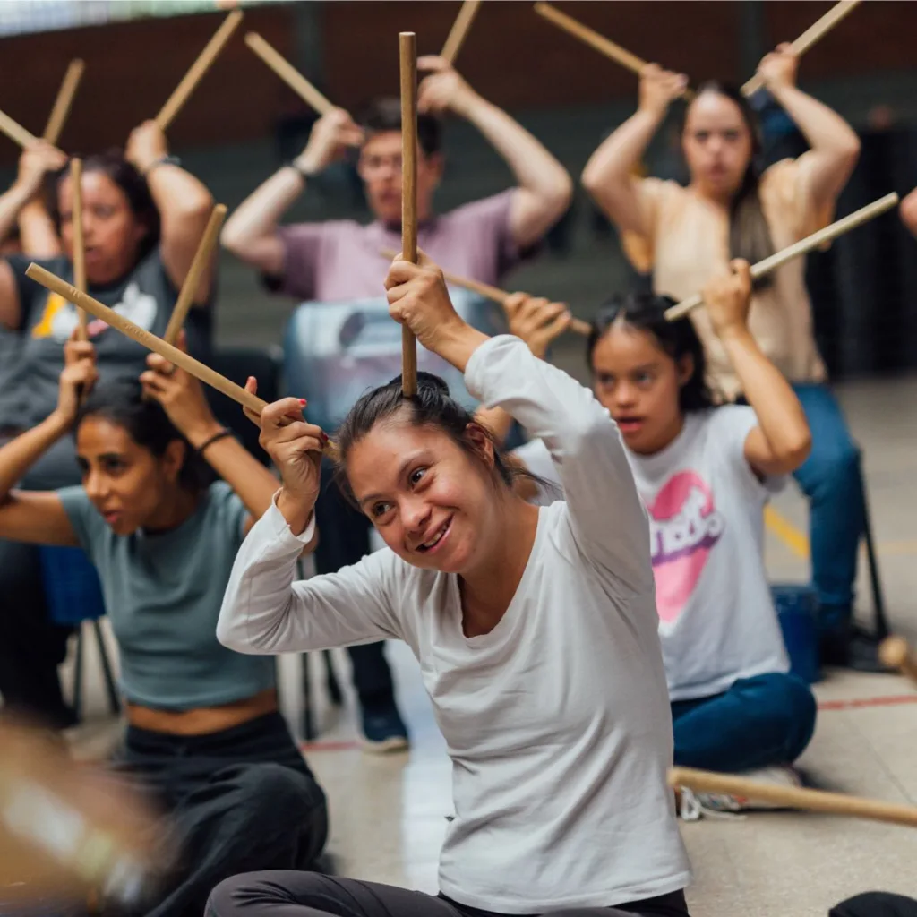 Joven con discapacidad sonriente participando en una actividad rítmica con baquetas durante un taller del programa Soy Músico de la Orquesta Filarmónica de Medellín
