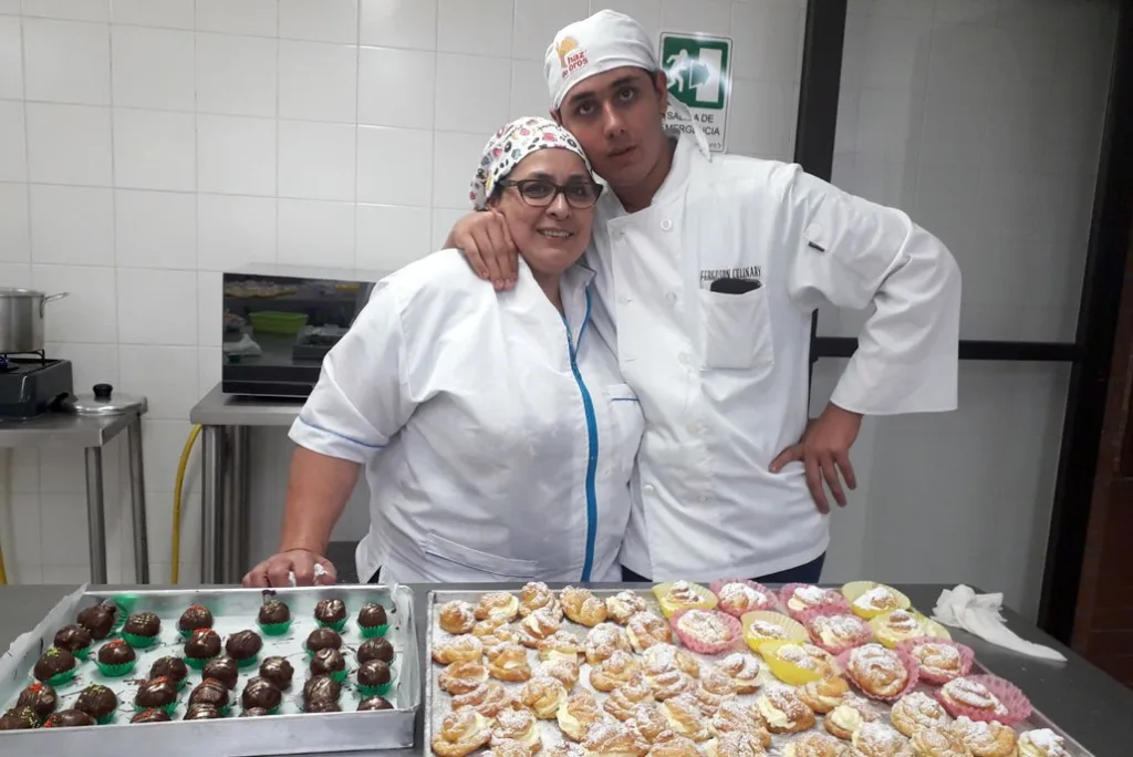 Tomás y su instructora de cocina posan sonrientes junto a bandejas con postres preparados por ellos