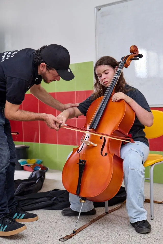 Profesor enseña a una joven cómo tocar el violonchelo durante una clase del programa FilU de la Orquesta Filarmónica de Medellín.