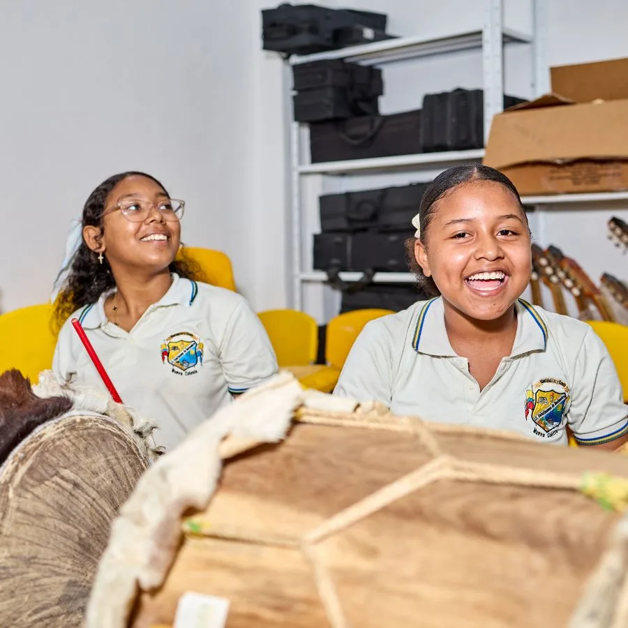 Dos niñas sonríen mientras tocan tambores durante una clase del programa FilU de la Orquesta Filarmónica de Medellín.