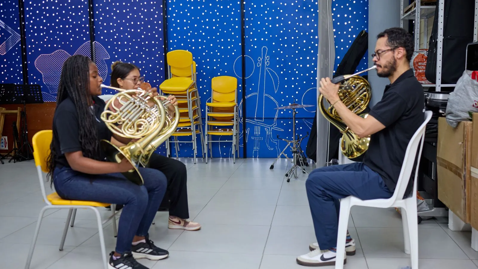 Tres personas tocan corno francés en una clase de música del programa FilU de la Orquesta Filarmónica de Medellín.