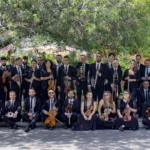 Todos los músicos que integran la Orquesta Filarmónica de Medellín posan sonriendo junto con su respectivo instrumento.
