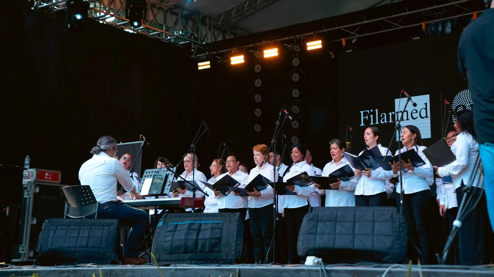 Coro Reconciliación de la Filarmónica de Medellín cantando en un escenario al aire libre junto a un pianista.